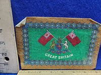 Front side of the cigarette felt showing coat of arms, two red flags, and 'GREAT BRITAIN' text with ruler for size reference.