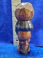 Side view of the hand carved wood sculpture showing the head and upper torso with a ruler for size reference.