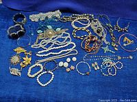 Full lot photo showing a variety of costume jewelry items including necklaces, bracelets, earrings, and brooches laid out on a blue surface.