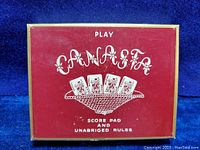 Box cover with red background, white text, and illustration of playing cards in a net design labeled as Canasta game set.