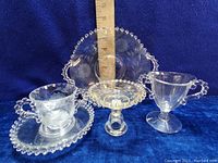 Group photo showing the four Candlewick pieces including the creamer with saucer, footed candy dish, and handled serving plate.