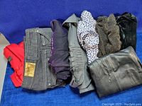Photo displaying a collection of seven folded garments including a red blazer, dark denim jeans with brand patch, and various skirts and dresses