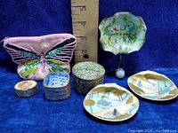 Overview of vintage lot with various trinket pots, hand-painted shell dishes, metal hook, and beaded butterfly purse on a blue background with ruler for scale.