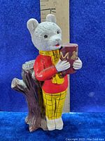 Full view of the vintage Rupert Bear vinyl figure showing clothing details and tree stump stand with ruler for size reference.