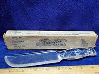 Photo of vintage Vitex Glas glass knife with original box placed behind it on blue fabric. The glass knife is clear with star design on handle and flat blade.