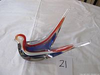 Side angle view of the glass bird figurine showing blue, red, and white swirls within clear glass, and the elongated tail design.