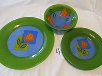 Green glass dinner plate, salad plates, and bowls with a flower design on a blue and green background.