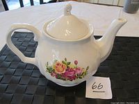 Side angle photo showing the teapot with red and yellow rose floral design and handle