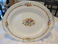 Oval cream-colored china platter with floral decoration in center and along the edge, placed on a white tablecloth with a stand holding it upright