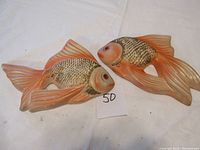 Two pink and cream colored fish-shaped chalkware wall decorations shown side by side on a white surface.