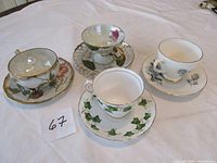 Set of four bone china teacups with matching saucers each with distinct floral or leaf patterns and gold trim detailing.