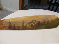 Side view of wooden paddle showing detailed hand painted naturalistic deer and woods scene.
