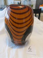 Photo showing front view of the swivel patterned handblown glass vase primarily in colors orange and black.