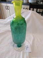 Full view of the green to yellow gradient tall glass decanter on clear round base, showing intact form except broken handle.