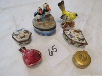 Overview of six trinket boxes including butterfly decorated porcelain enamel boxes, bird figurine boxes (cardinal, pelicans, yellow bird), and gold-tone metal box.