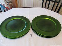 Stack of ten green charger plates on a white tablecloth, showing color and shape clearly.
