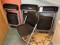 Group of black folding chairs stacked and one opened, showing the plastic seat and metal frame construction.
