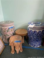 Two ceramic garden stools painted in blue and white and pink and green botanical colors, alongside a wooden elephant stool and small wooden round stool.