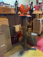 Full front view of orange Central Machinery bench grinder mounted on metal pedestal stand in workshop setting.