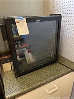 Avanti mini beverage fridge on countertop, front view showing black frame and glass door with tag