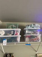 Wide view of five plastic storage bins stacked on a shelf containing various Christmas decorations.