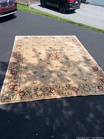 Floral area rug laid out on driveway showing the full pattern with a cream background, central floral medallion, and detailed floral border.
