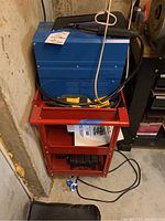 Welder on red wheeled cart in basement workshop