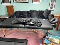 Full view of the massage table set up with black cushioned surface and black cover on top, wooden legs visible.