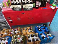 Front view of red metal cabinet with two doors, surface with beverage items not included in sale, blue and brown shopping bags with bottles on floor.