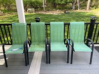 Four green tone outdoor chairs with black metal armrests and frames on a porch deck, showing signs of use and some dirt.