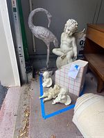 Photo showing all the statues together in a garage corner, including one large metal crane and four angel statues (one large, three smaller).