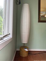 Full view of tall floor lamp with white paper shade near window on hardwood floor