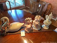 Wide shot of all four figurines on a wooden dining table: three angels and one swan with wreath.