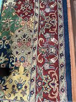 Close up of the rug border showing intricate floral design in red and blue earth tones along the edge on wood floor.