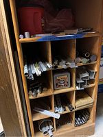 Photo showing the wooden cubby organizer with divided compartments filled with metal pieces including round rods, square bars, angle bars, smaller metal parts, and a red Folgers container used for storage.