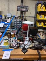 Overall bench layout showing soldering station, lamp, multimeter, heat gun and spools