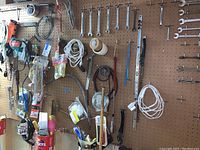 Wide view of pegboard with assorted tools including hammers, cords, cables, tubing, tape, and various smaller hand tools hanging on hooks.