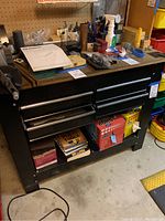 Front view of black metal workbench showing four drawers, wooden top and open bottom shelf