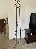 Full view of black metal art easel standing near wall and furniture