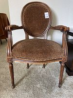 Front view of wood framed chair with brown designer fabric upholstery, showing carved armrests and legs.
