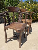 Two solid wood Chinese corner chairs shown outdoors with visible carved decorative side panels, curved backs, and wooden seats. Both chairs appear disassembled or in need of reassembly and repair.