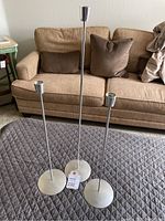 Front view of three Danish steel candlesticks in varying heights on a quilted surface in front of a beige sofa.