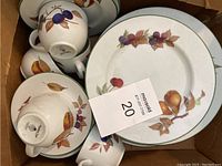 Photo showing stacked plates and several tea cups with fruit and leaf patterns on white ceramic with green rim.