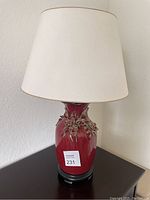 Full view of the vintage lamp showing the red ceramic base with floral relief and white fabric lampshade on top.