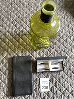 Green glass jar, black leather travel pouch, and Pierre Cardin pen set box with pens inside on a quilted surface