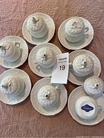 All 8 white ceramic pot de la cremes with matching saucers, arranged on fabric surface, showing overall set condition and arrangement.