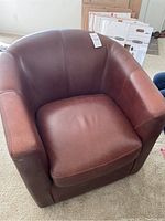 Front view of one brown leather swivel club chair with removable seat cushion and curved arm/back design