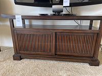 Front view of dark wood TV cabinet with slatted sliding doors below and open shelf on top.