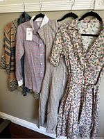 Photo of the lot showing three hangers with a plaid shirt, a plaid dress, and a floral wrap dress hung on a wall.