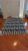 Rectangular navy and beige circle patterned area rug placed in front of a door on hardwood floor. Shows overall pattern and condition of the rug.
